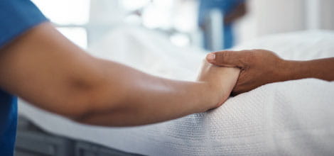 Nurse holding hands of patient at hospital bedside after cancer diagnosis